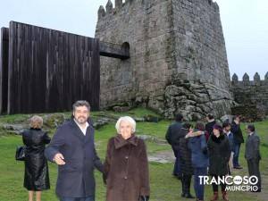 Grupo de pessoas em frente a castelo medieval de pedra com torre e muralhas, em zona de relva.