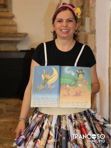 Mulher com headband rosa segurando livro aberto com ilustrações coloridas de personagens infantis.