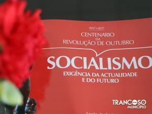 Cartaz vermelho com texto sobre centenário da Revolução de Outubro de 1917-2017 e socialismo, com flor vermelha em primeiro plano