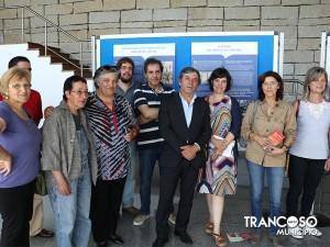 Grupo de aproximadamente dez pessoas posando junto a painel azul com textos informativos, em espaço interior com parede de tijolos.