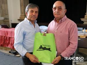 Dois homens seguram um saco verde com logótipo Trancoso durante evento de apresentação de livro.