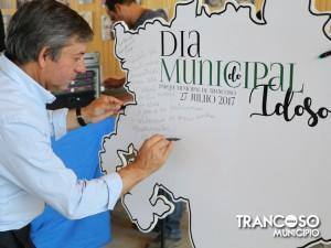 Homem de camisa azul clara e avental azul assinando painel com inscrições sobre Dia Municipal do Idoso, 27 de julho de 2017.