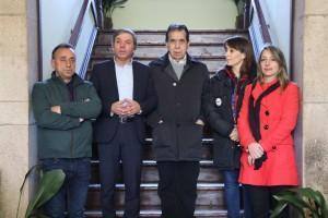 Cinco pessoas posicionadas numa escada de madeira, envolvidas numa reunião ou sessão oficial, com janelas e plantas ao fundo.
