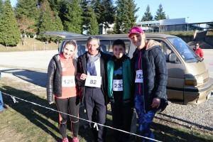 Quatro participantes de prova desportiva posam juntos junto a uma carrinha, com coletes de número visíveis.
